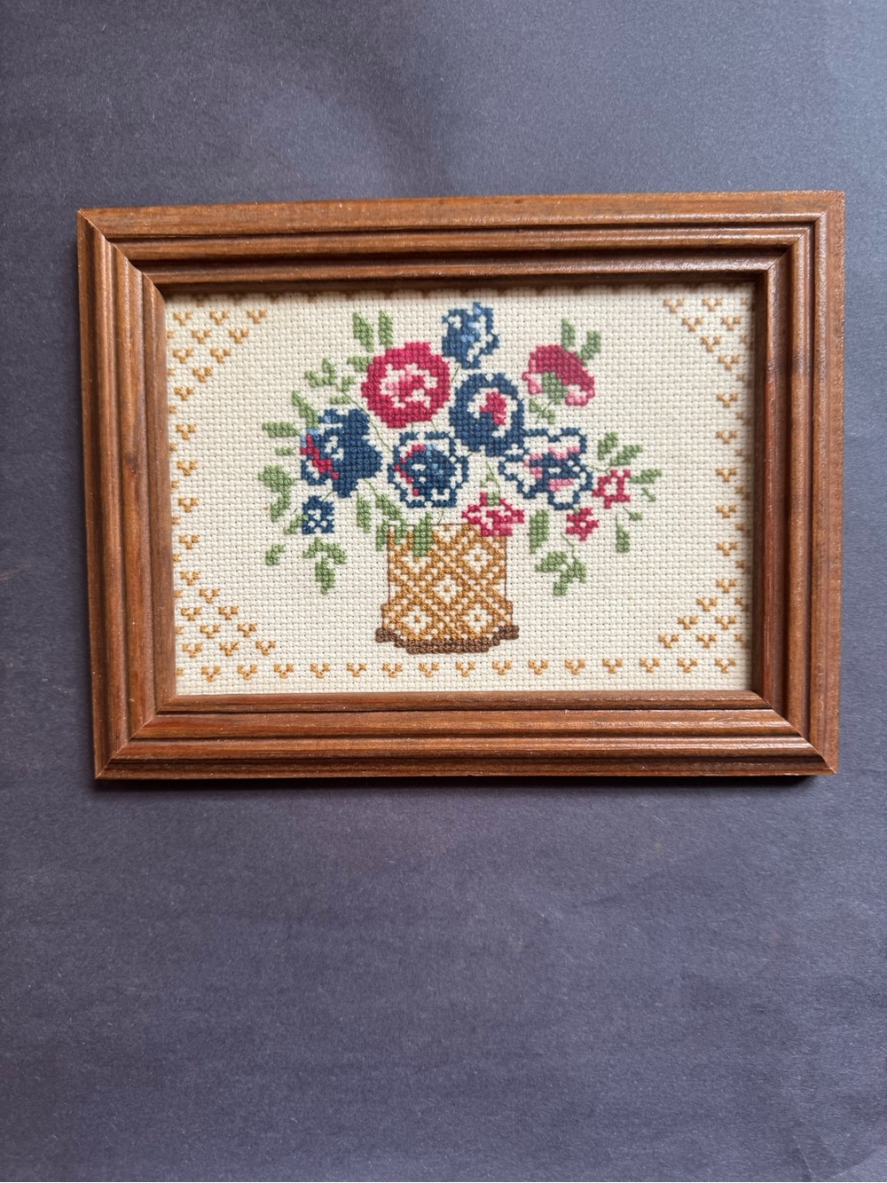 Framed cross-stitch with a colorful floral bouquet in a wicker basket